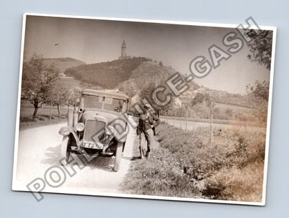Stará fotografie muž s autem a věží na kopci (BM26424)