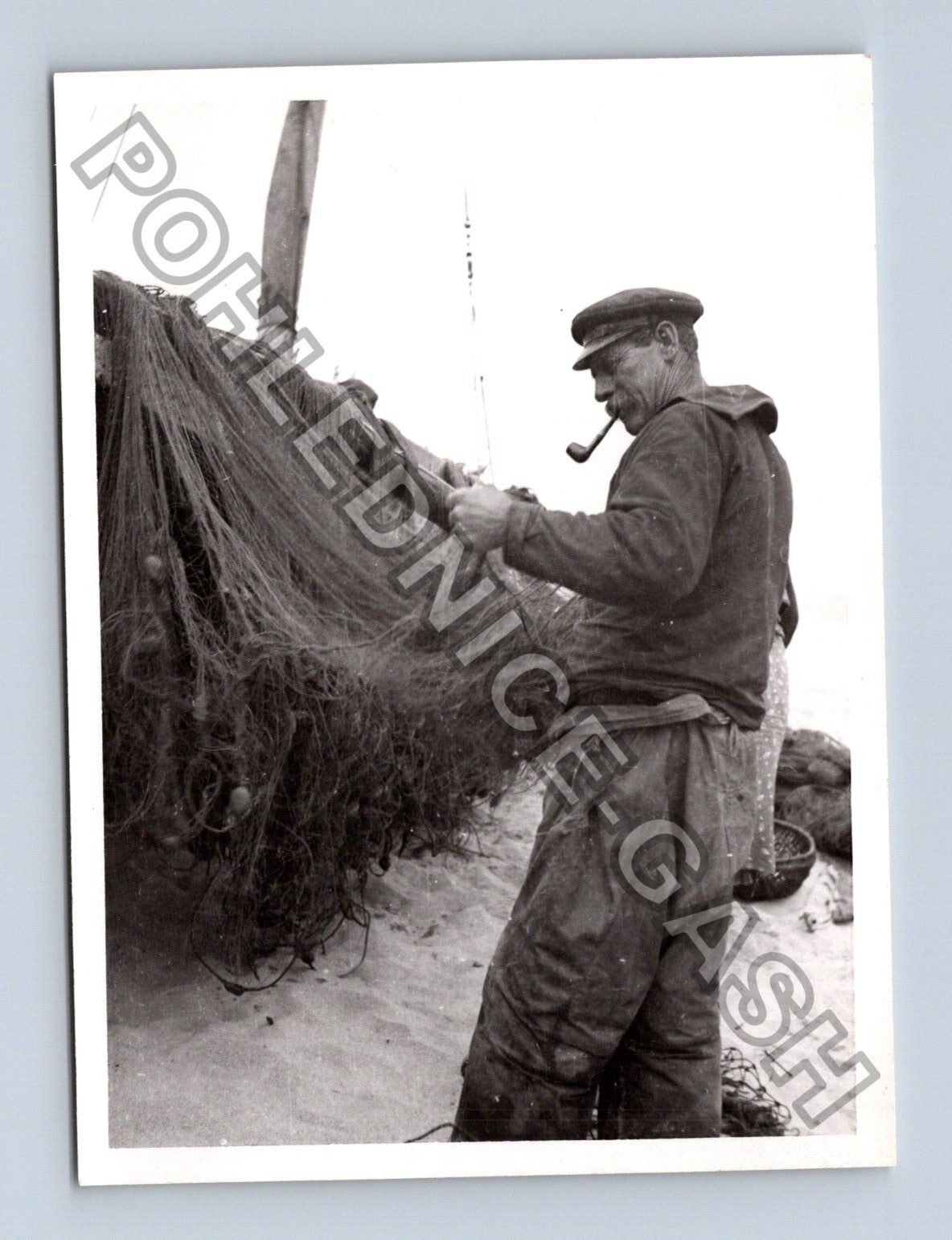 Stará fotografie rybář s dýmkou opravuje sítě na pláži (BM26875)