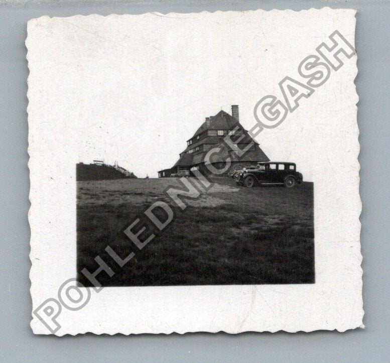 Stará fotografie budova s autem v kopcovité krajině (BM26959)