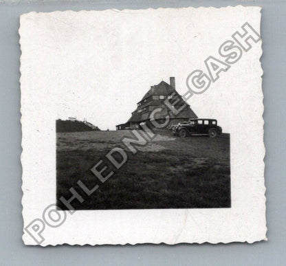 Stará fotografie budova s autem v kopcovité krajině (BM26959)